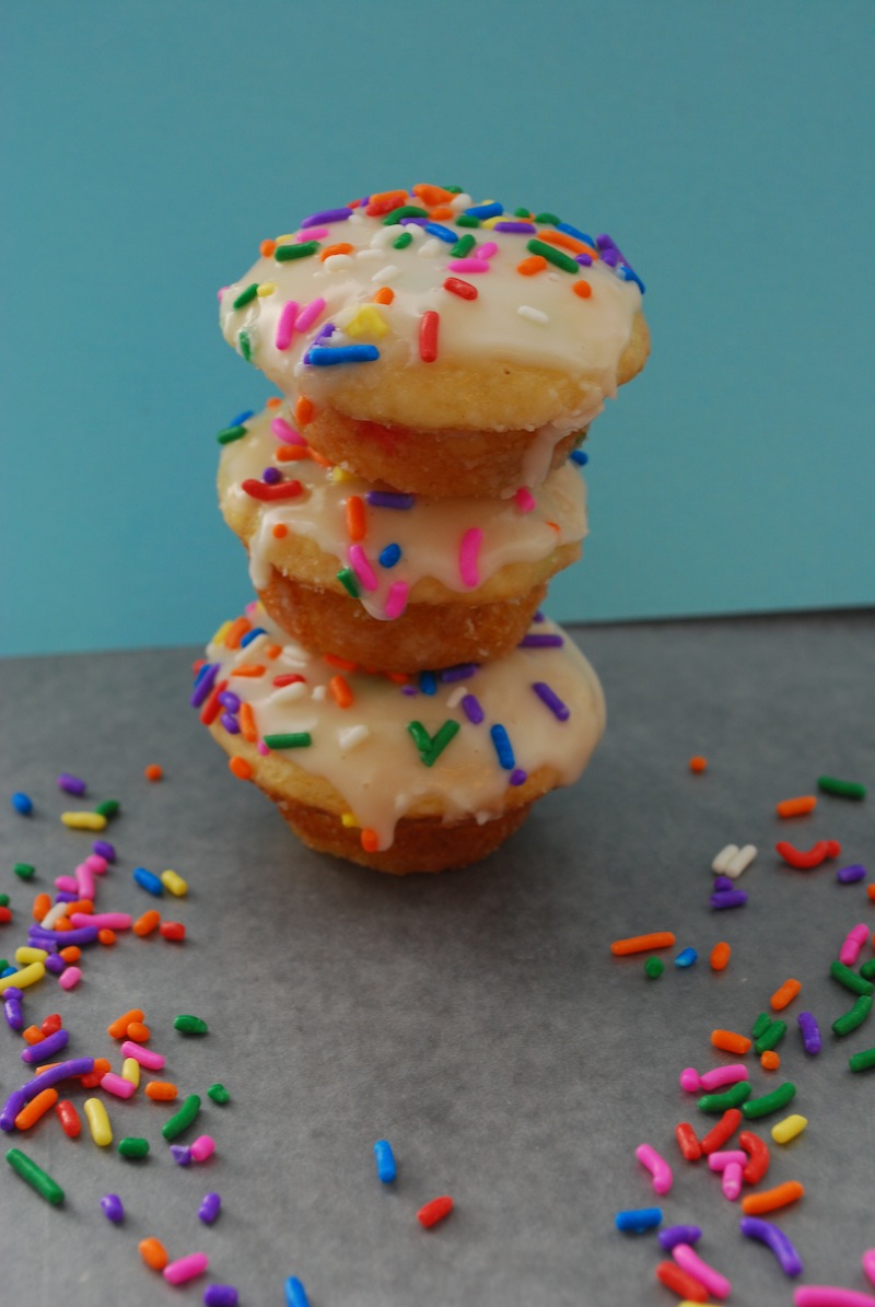 A stack of three twice-glazed Funfetti cake donuts surrounded by sprinkles