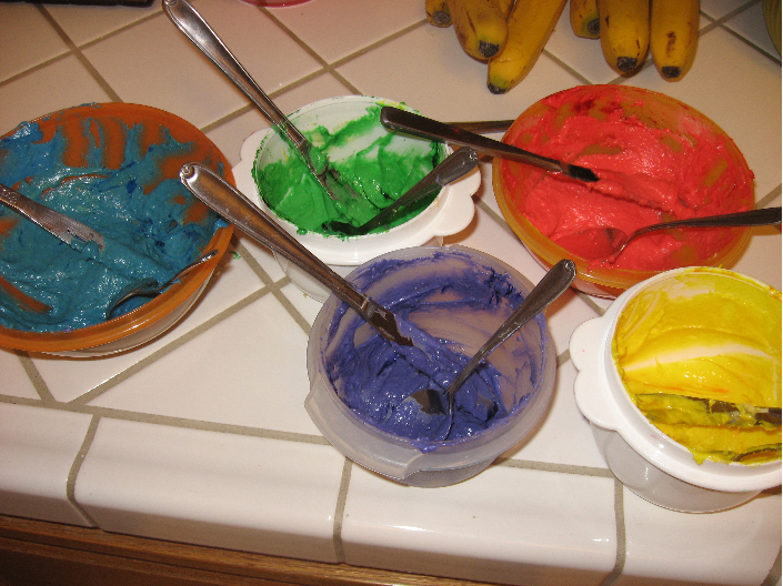 Five bowls with blue, green purple, red, and yellow dyed cupcake batter