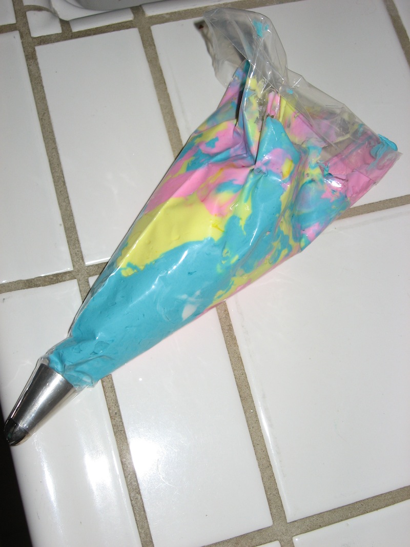 A frosting dispenser filled with blue, yellow, and pink marbled frosting