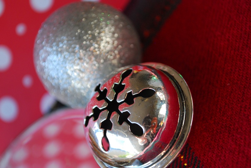 A silver bell and a silver glitter holiday bauble on a red holiday themed backdrop