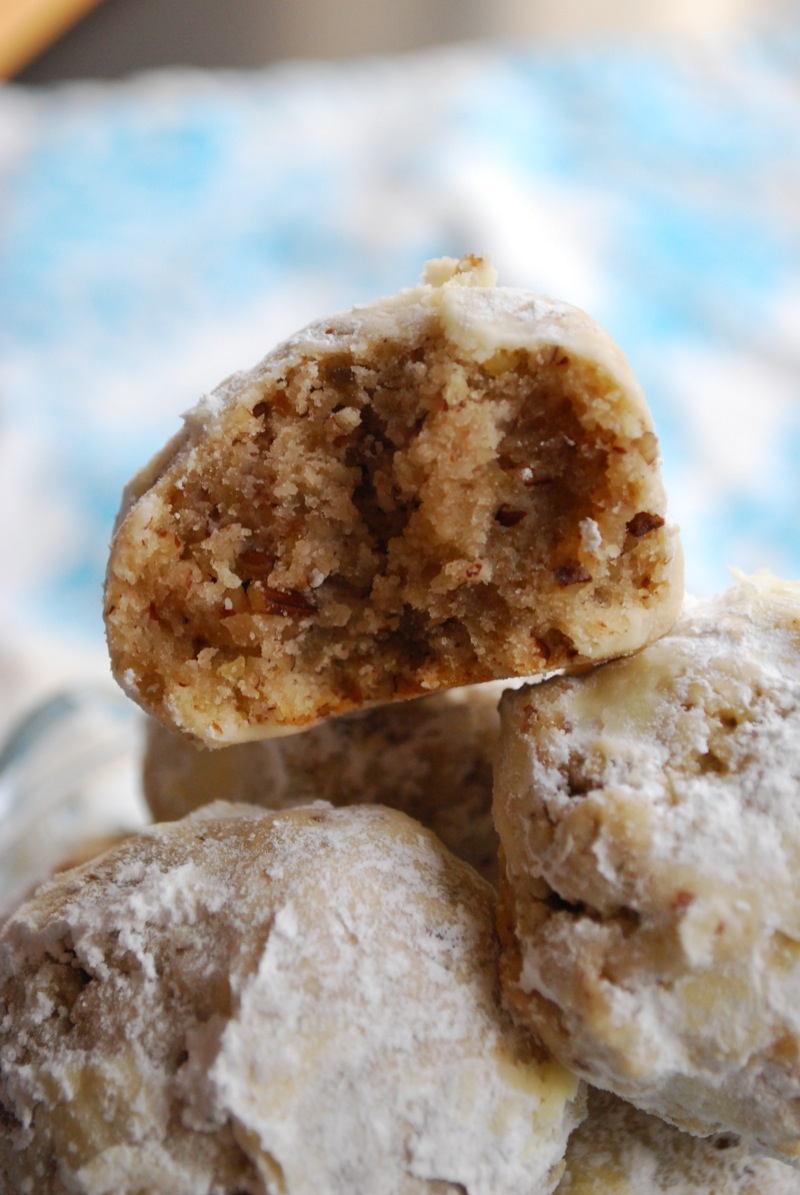 Close-up of pecan snowball cookies with one bitten in half to show the texture