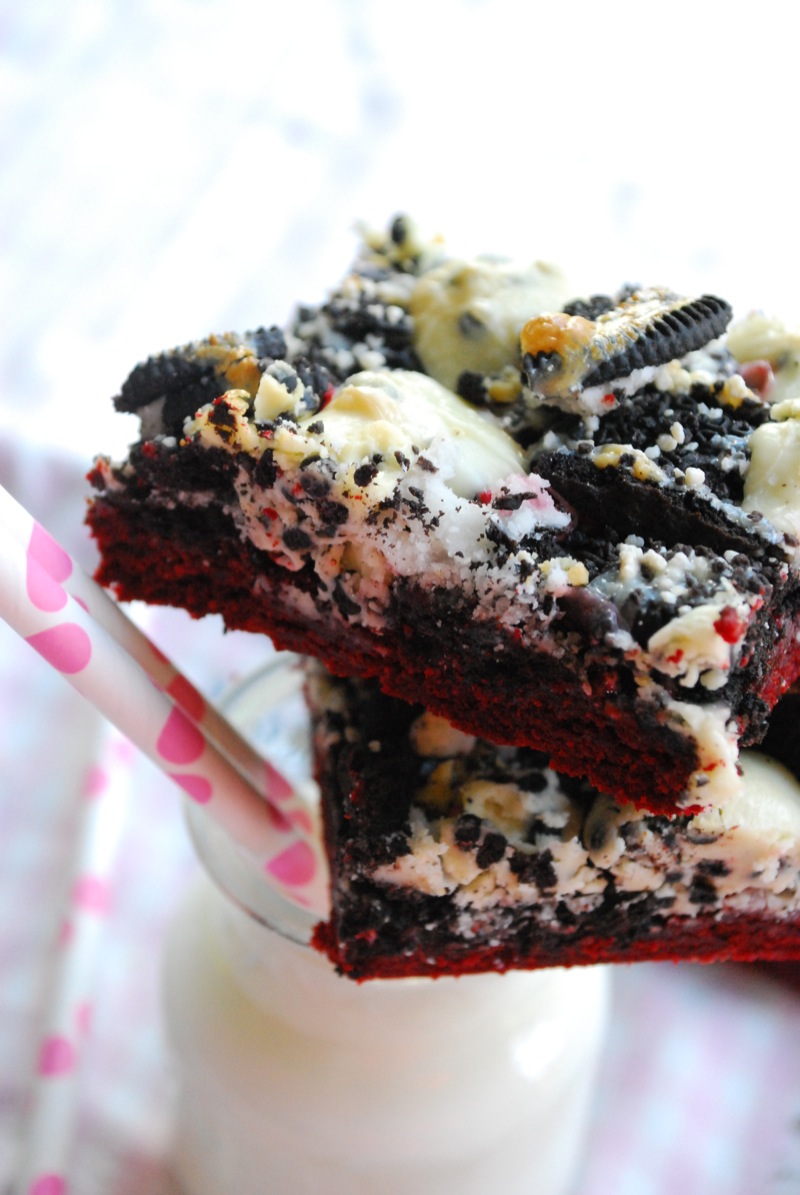 close up of red velvet cookies & cream magic bars sitting on a glass of milk with a pink straw