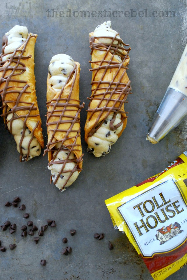 chocolate chip cookie dough cannolis on a metal baking sheet with chocolate chips and a piping bag
