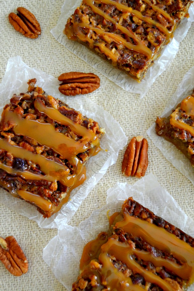 salted caramel pecan pie bars arranged with pecans on light fabric and parchment