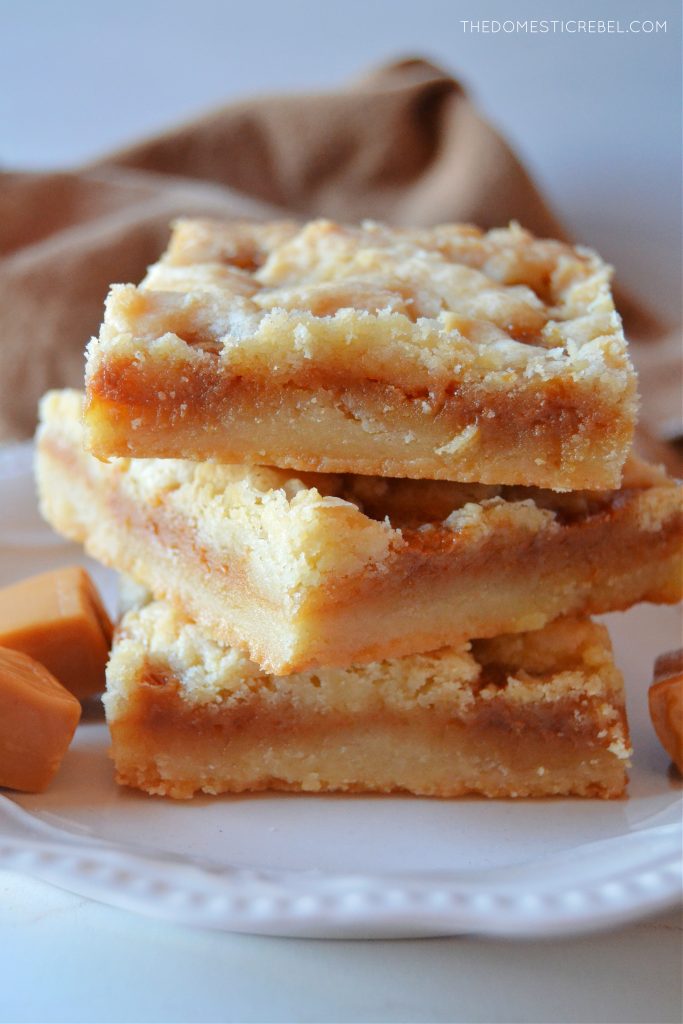 a three-high stack of salted caramel butter bars on a small white plate. little caramel square candies sit next to them on the plate.