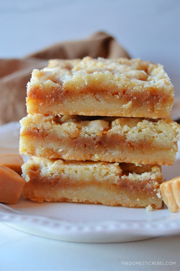 a three-high stack of salted caramel butter bars on a petite white plate next to caramel square candies. 