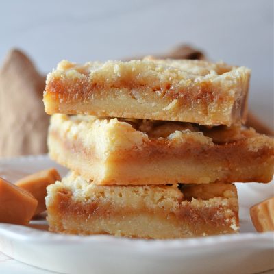 a trio stack of salted caramel butter bars on a white plate with little caramel squares next to them.