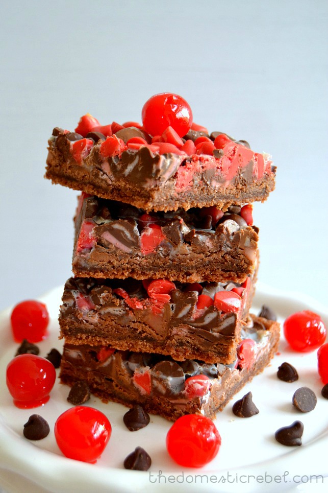 chocolate cherry seven layer bars stacked on white plate surrounded by cherries and chocolate chips