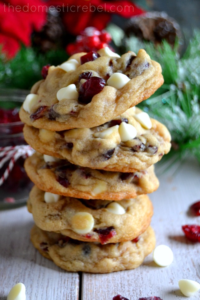 white chocolate cranberry cookies stacked on white background with pine in background