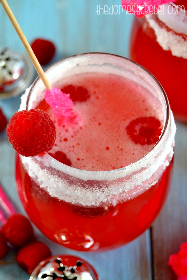 Raspberry Candy Champagne Punch in a glass with a rock candy stirrer and fresh raspberries
