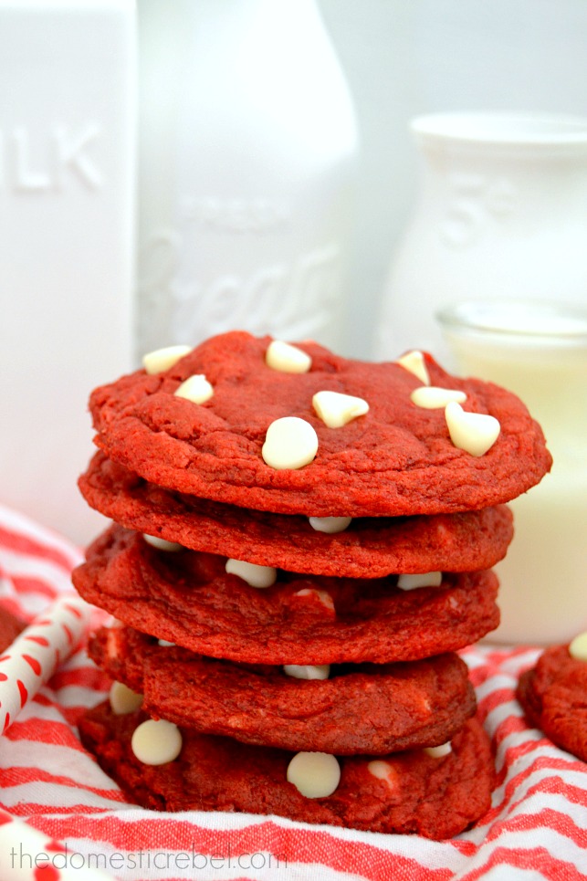 Red Velvet Cookies stacked on red fabric against white milk glasses in background