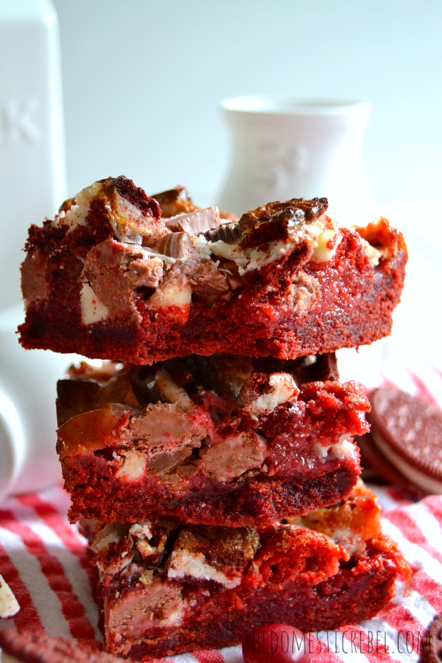 Red Velvet Seven Layer Bars stacked with a bite removed and milk bottles in background