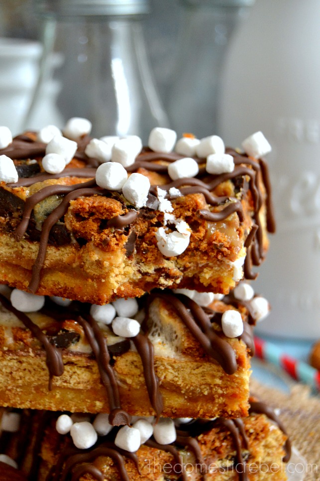 Biscoff Smores Seven Layer Bars stacked with bite mark in front of glass bottles