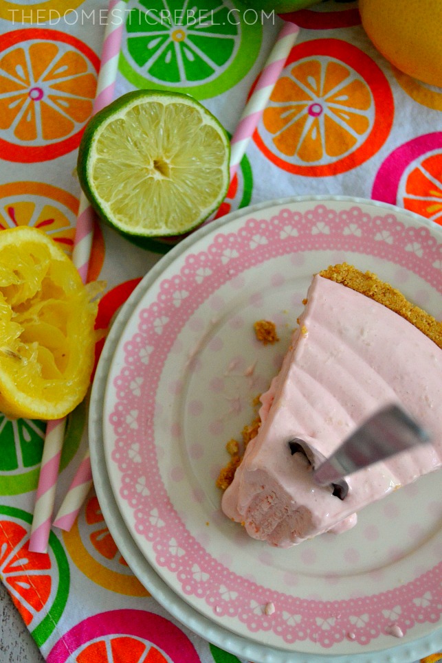 shot of pink lemonade cheesecake pie slice on plate with limes, lemons and straws next to it