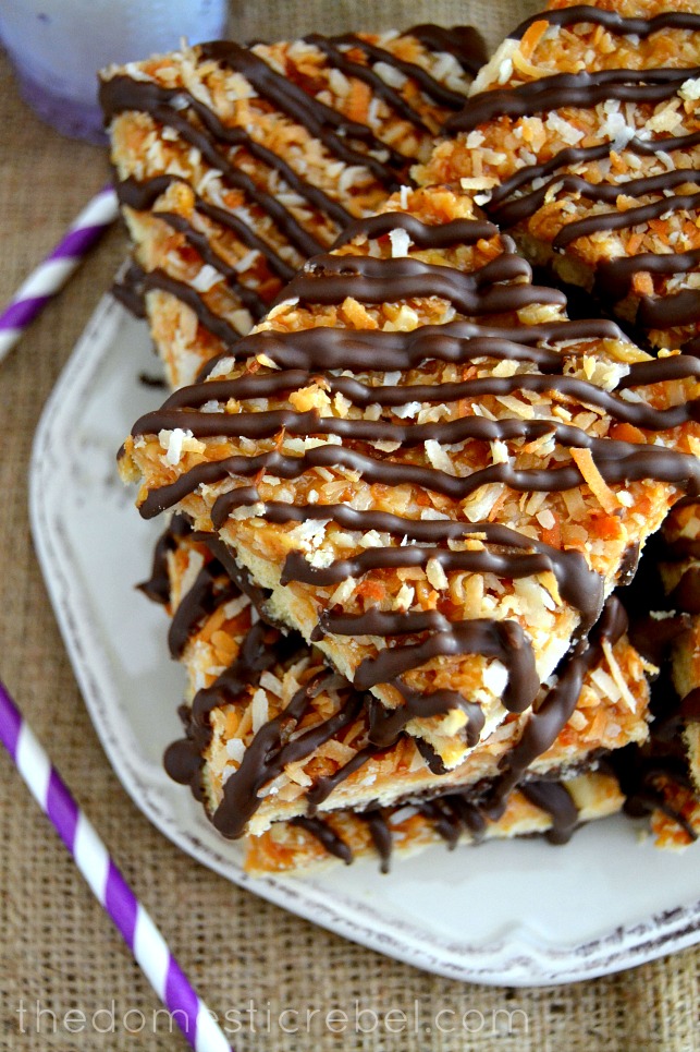 sugar cookie samoas bars stacked on white plate with purple straws in background