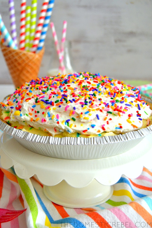 funfetti cream pie on cake stand with rainbow fabric and rainbow straws in background
