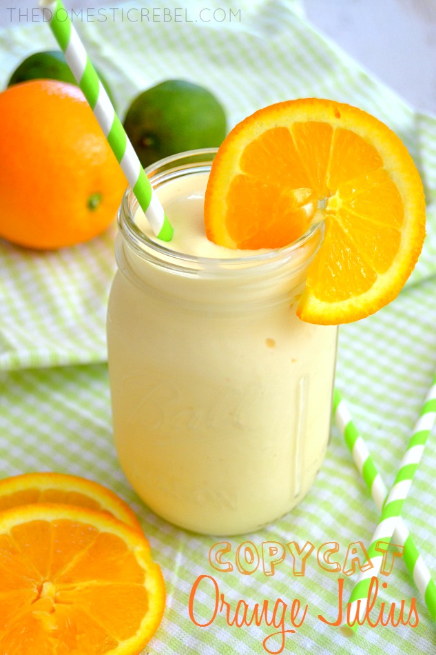 copycat orange julius with fresh orange slices and a green straw on green fabric
