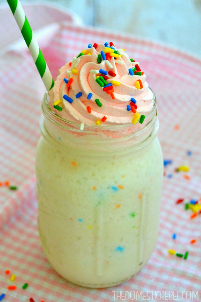 birthday cake frappuccino in a glass with sprinkles, a green straw and a pink background