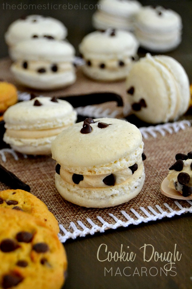 cookie dough macarons on dark wood background with cookies and mini chocolate chips