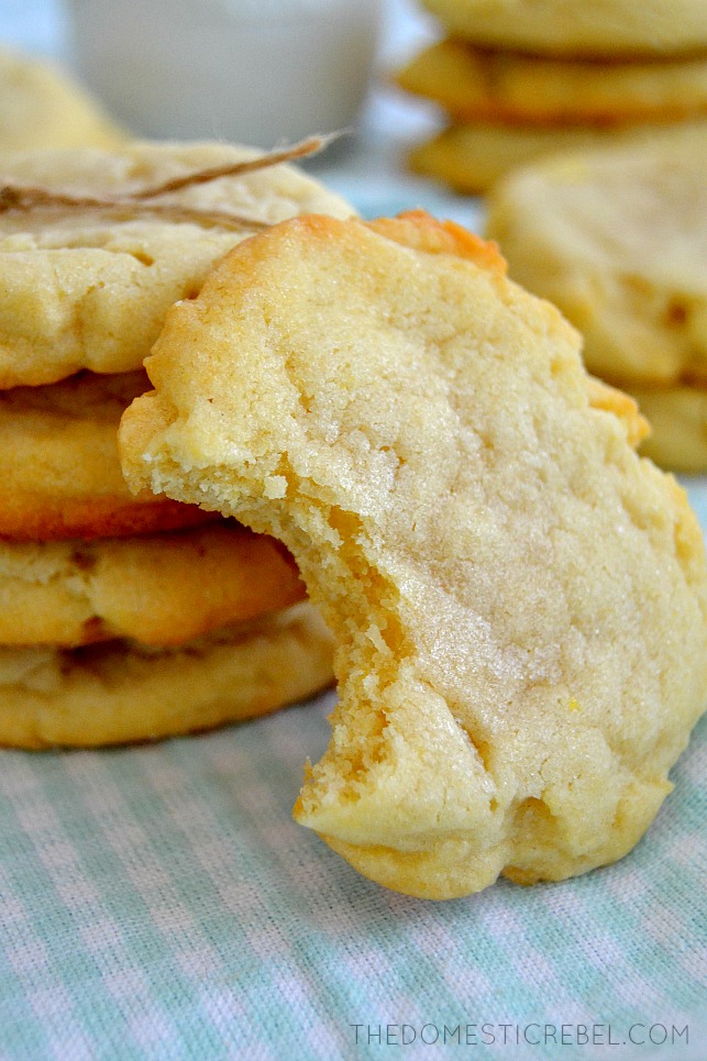 Old-Fashioned Sugar Cookies with bite missing propped on stack of cookies and blue background