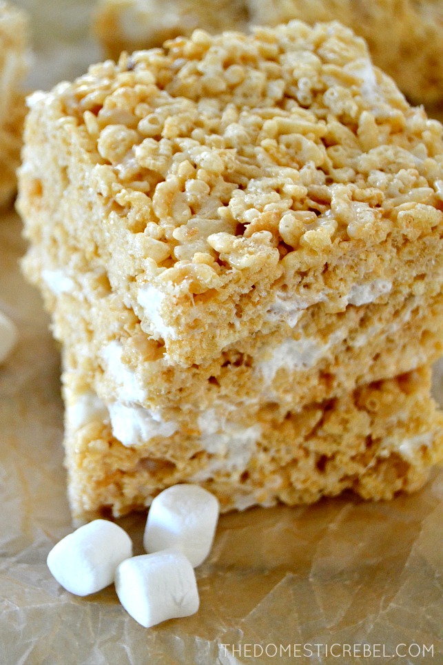 Rice Krispy Treats stacked on brown parchment with marshmallows