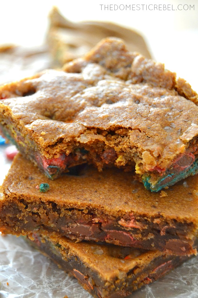 Brown Butter Espresso M&M Blondies stacked with bite missing on parchment paper