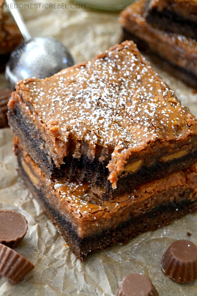 Chocolate PB Gooey Bars stacked with bite missing on parchment with PB cups