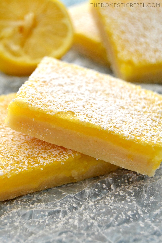 Closeup of Lemon Bars stacked on parchment with lemon wedge