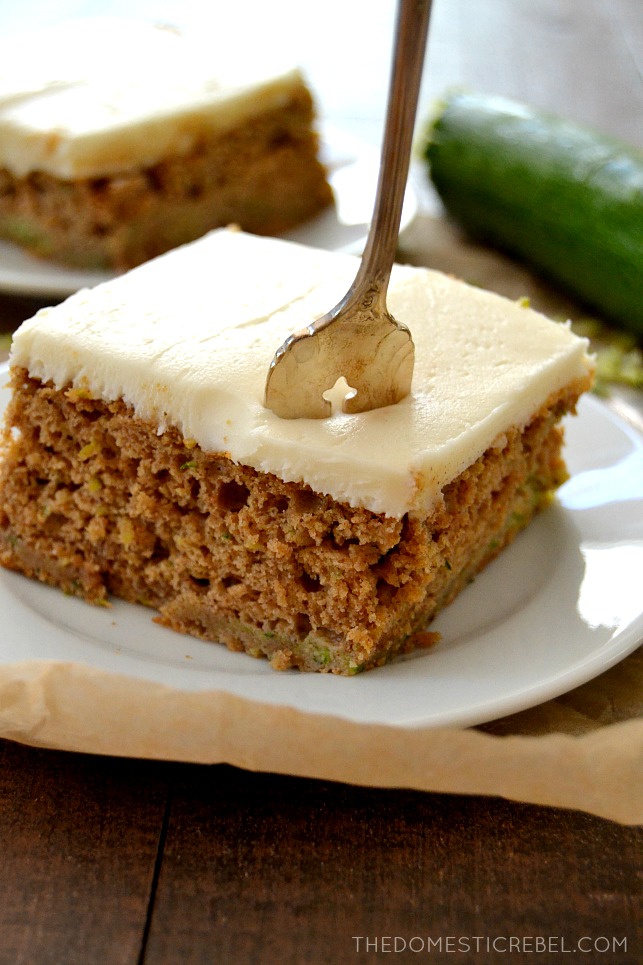 Zucchini Cake slice on white plate with fork in it with zucchini in background