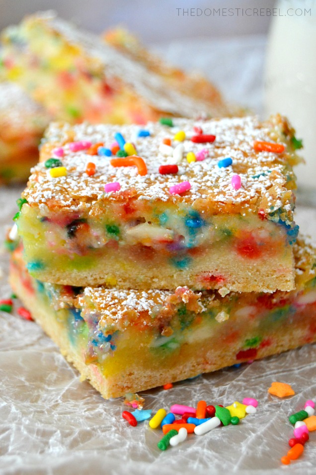 Closeup of Cake Batter Gooey Bars stacked on parchment with sprinkles