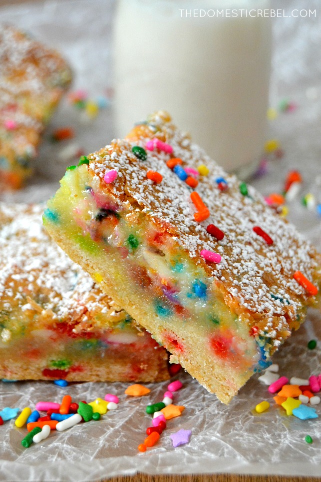 Cake Batter Gooey Bars arranged on parchment with sprinkles and milk