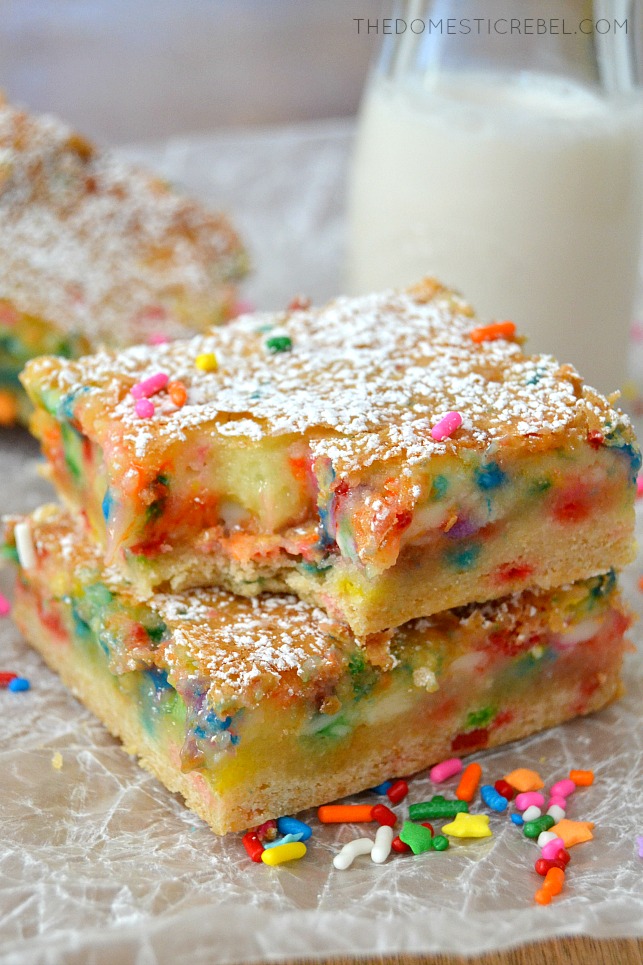 Cake Batter Gooey Bars with bite missing on parchment with sprinkles and milk