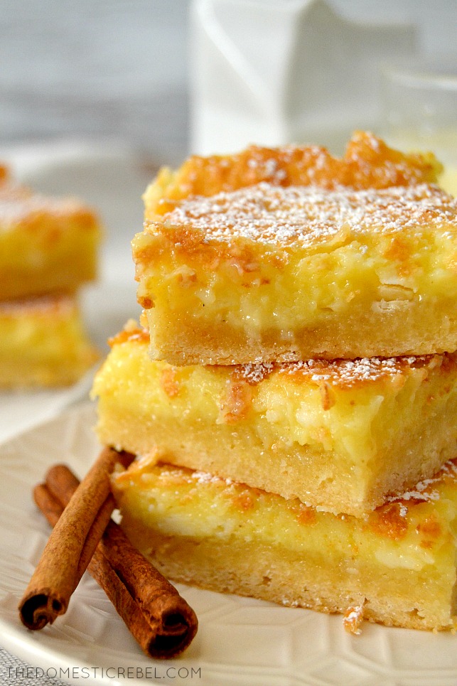 closeup of eggnog gooey bars stacked on white plate with cinnamon sticks