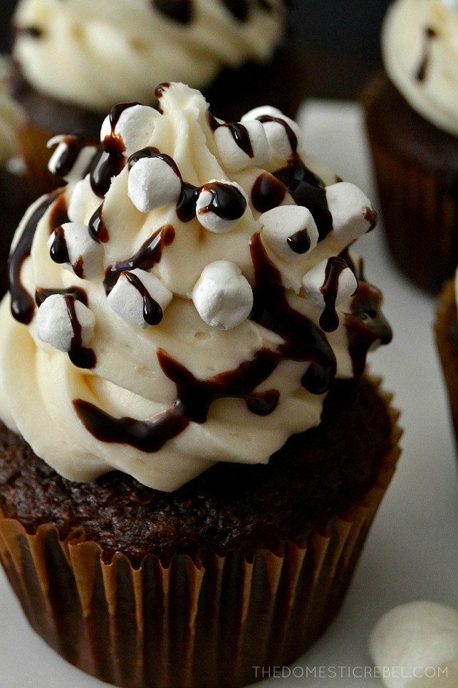 CLOSE UP OF A HOT CHOCOLATE CUPCAKE WITH CHOCOLATE DRIZZLE AND MINI MARSHMALLOWS.