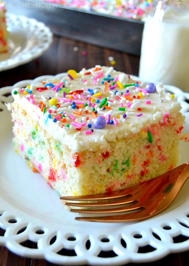 ONE SLICE OF FUNFETTI CAKE ON A WHITE PLATE WITH A FORK