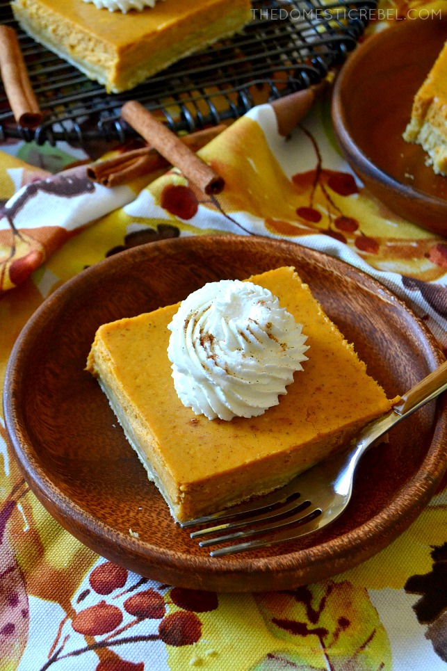 pumpkin cheesecake bar on a wooden plate with whipped cream and a fork
