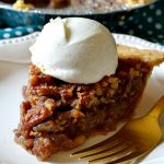 bourbon pecan pie slice with a huge dollop of whipped cream on top of a white lacy plate with a gold fork