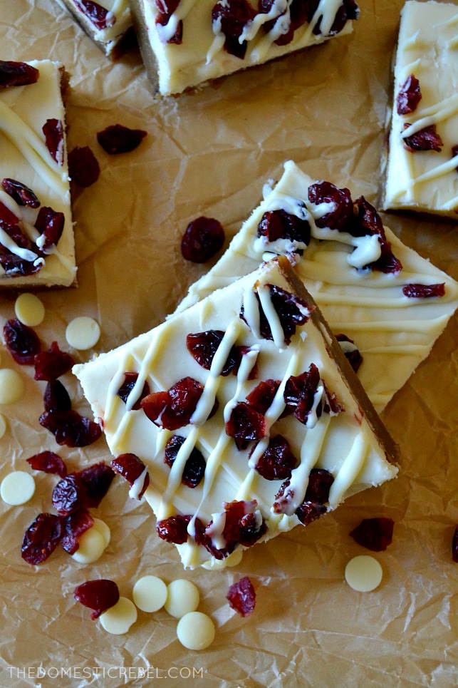 six cranberry bliss bars arranged on parchment with cranberries and white chocolate