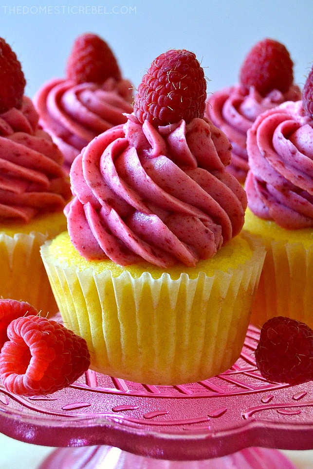raspberry lemonade cupcake on a pink glass cake stand next to fresh raspberries