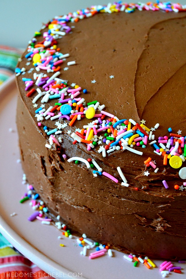 whole yellow cake with chocolate frosting topped with rainbow sprinkles