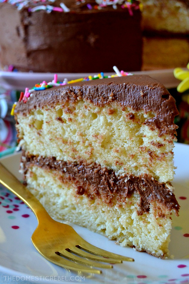 a slice of yellow cake with fudge frosting standing upright on a polka dot plate