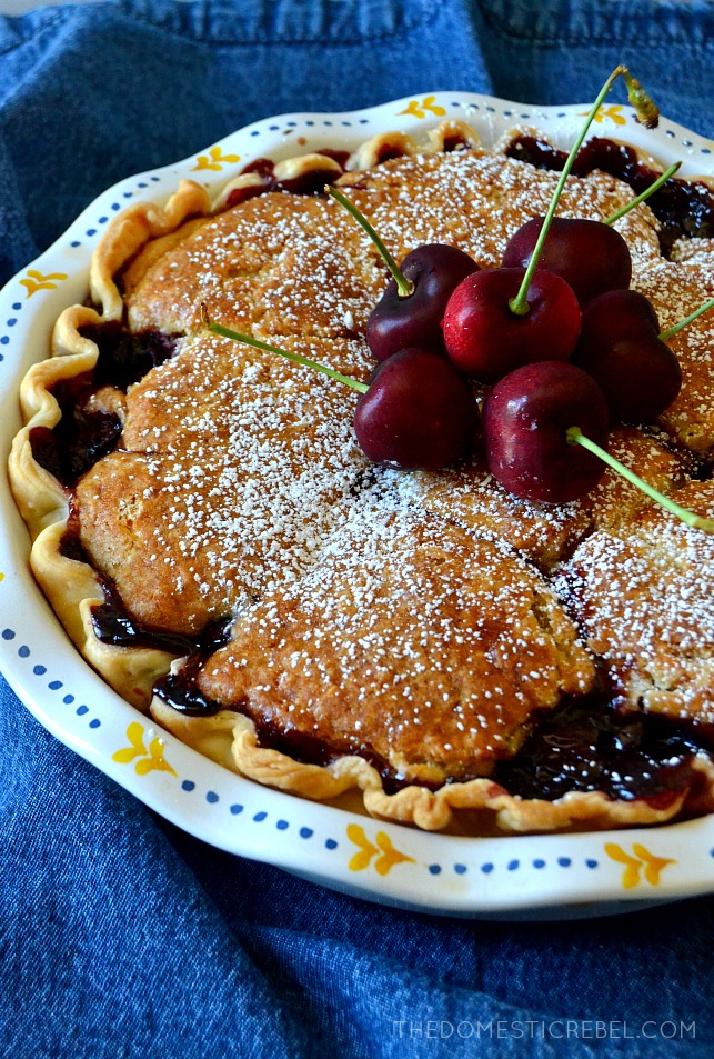 whole cherry cobbler pie in a pie pan topped with powdered sugar and cherries