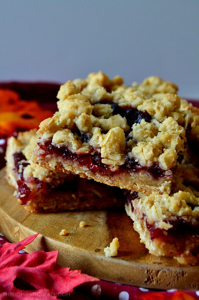 Three cranberry crumble bars stacked on a wooden slab