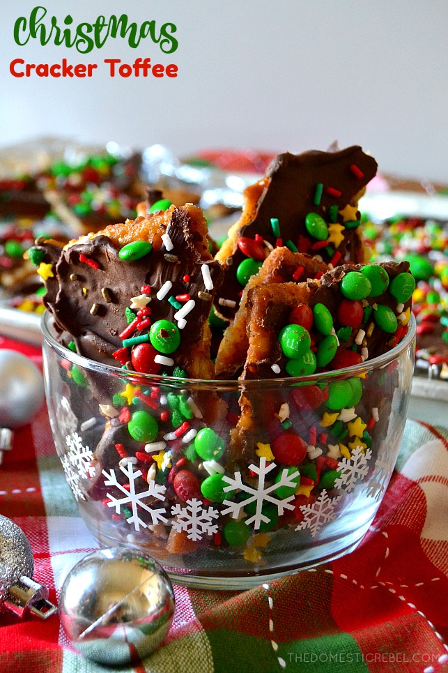 Pieces of Christmas cracker toffee in a clear bowl with snowflakes on the side on a holiday backdrop
