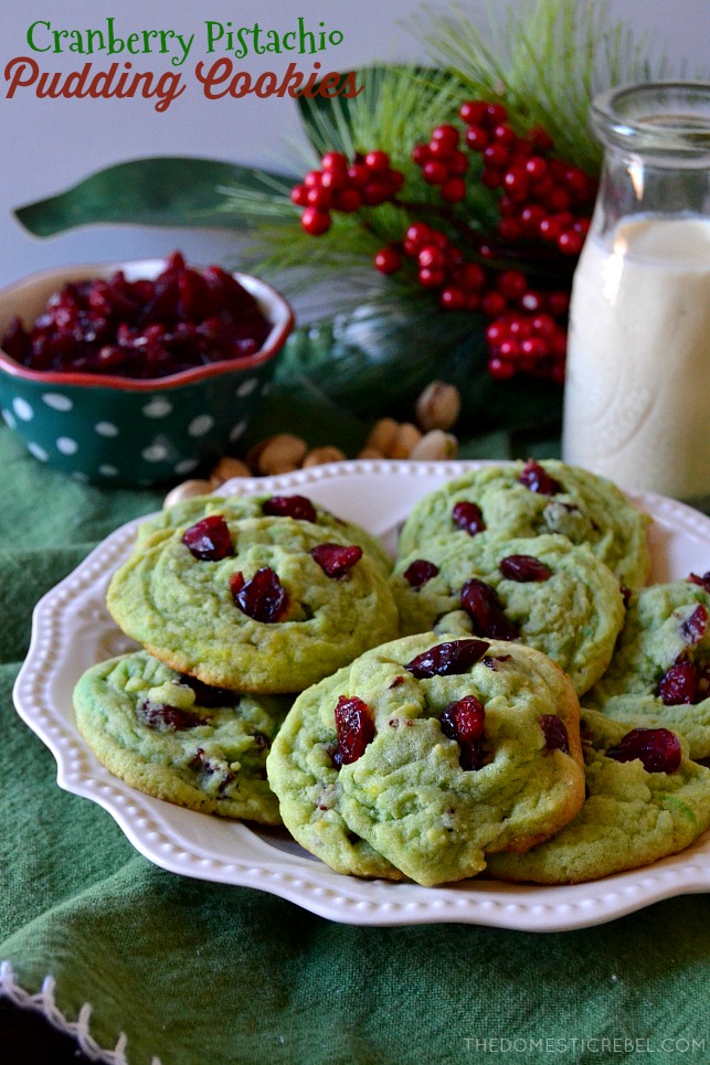 An array of cranberry pistachio pudding cookies on a plate in front of a glass of milk and holiday berries
