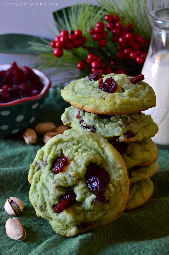 Six cranberry pistachio pudding cookies in front of a holiday backdrop with pistachios next to and behind them