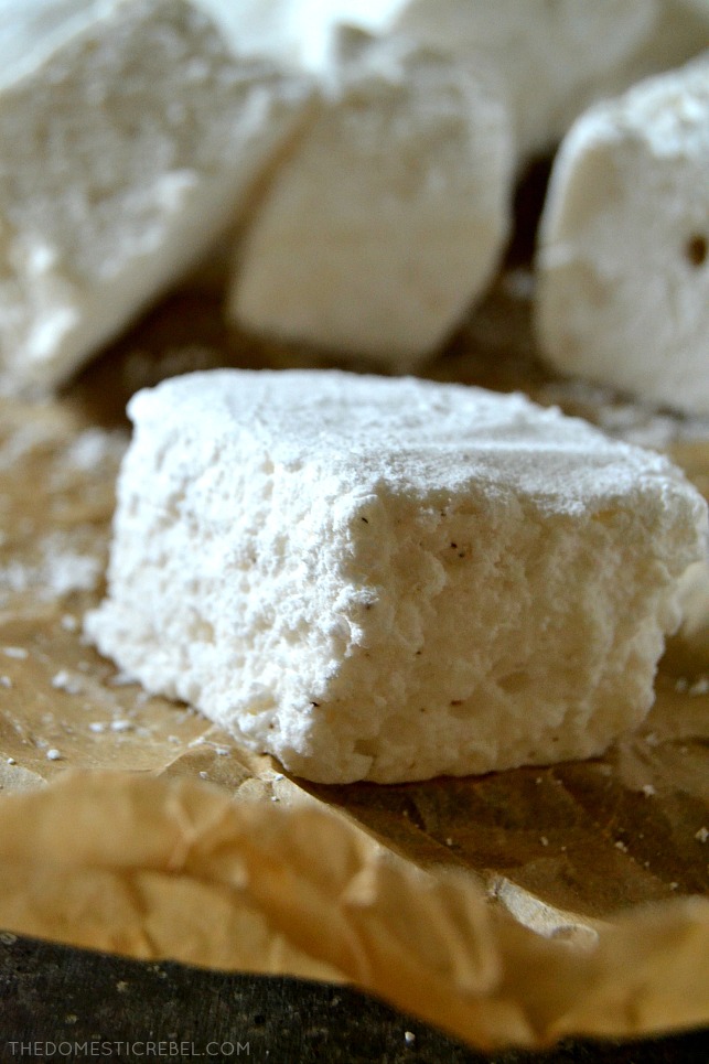 Close-up of a homemade marshmallow resting on brown parchment paper in front of more marshmallows