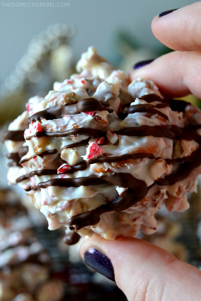 Close-up of a hand with blue glitter nails holding a piece of white chocolate peppermint bark pretzel candy