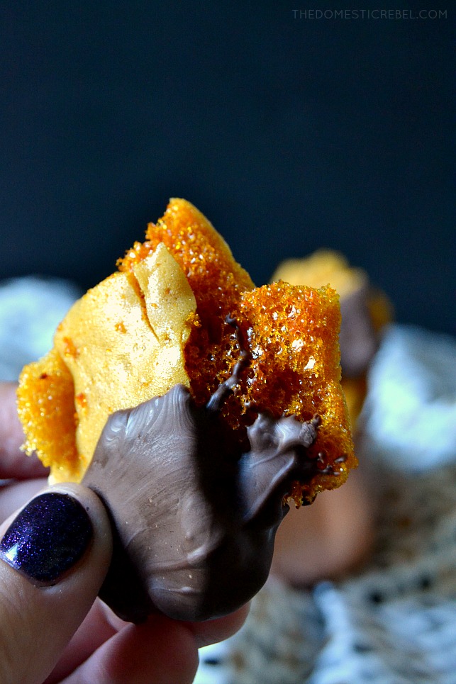 Close-up of fingers with blue glitter nails holding a piece of honeycomb sponge candy