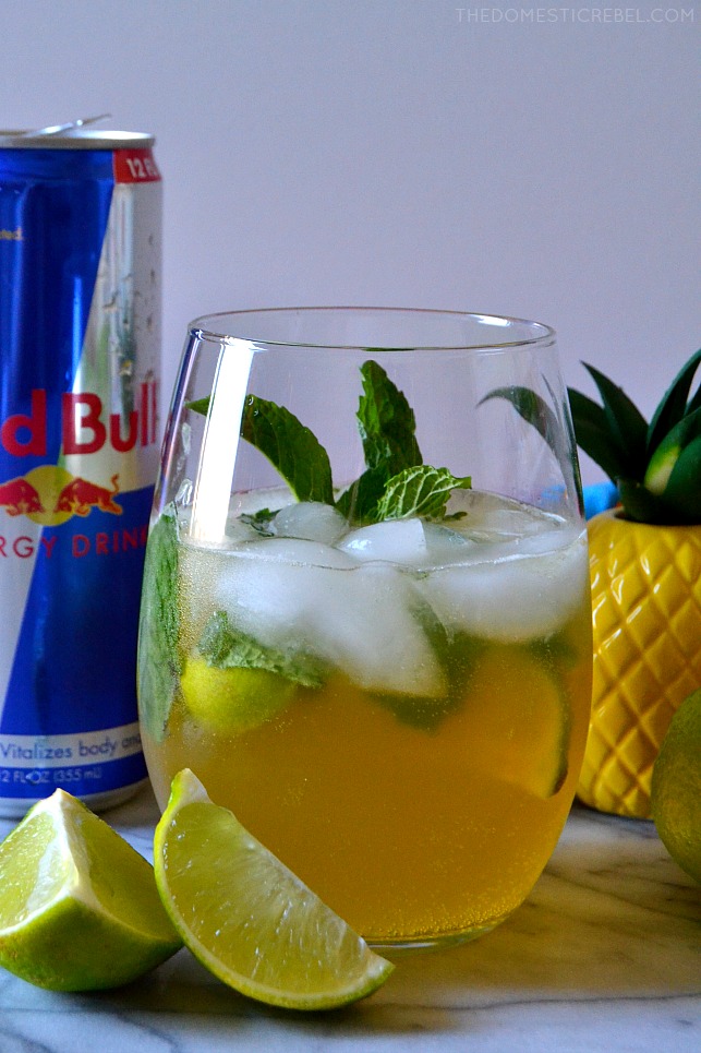 red bull pina cocojito in clear glass with lime wedges, pineapple and red bull can